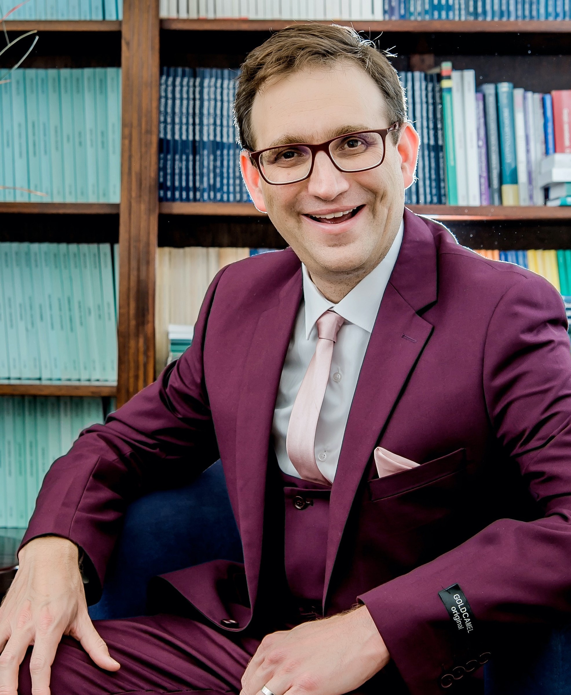 Professor Bilchitz wearing a plum suit and pink tie, sitting in front of a bookshelf.