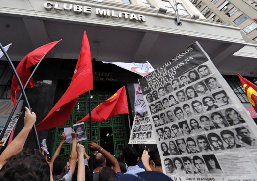 A photo of people holding a banner with pictures of the victims of torture and disappeared people at a protest in front of the Military Club in Brazil.
