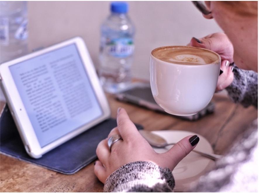 A woman drinking a coffee and reading an ebook.