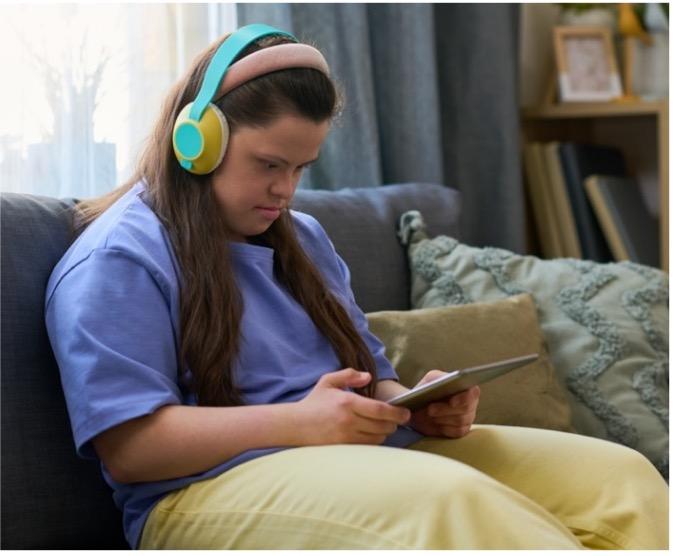 A young girl with Down syndrome using her tablet with headphones.