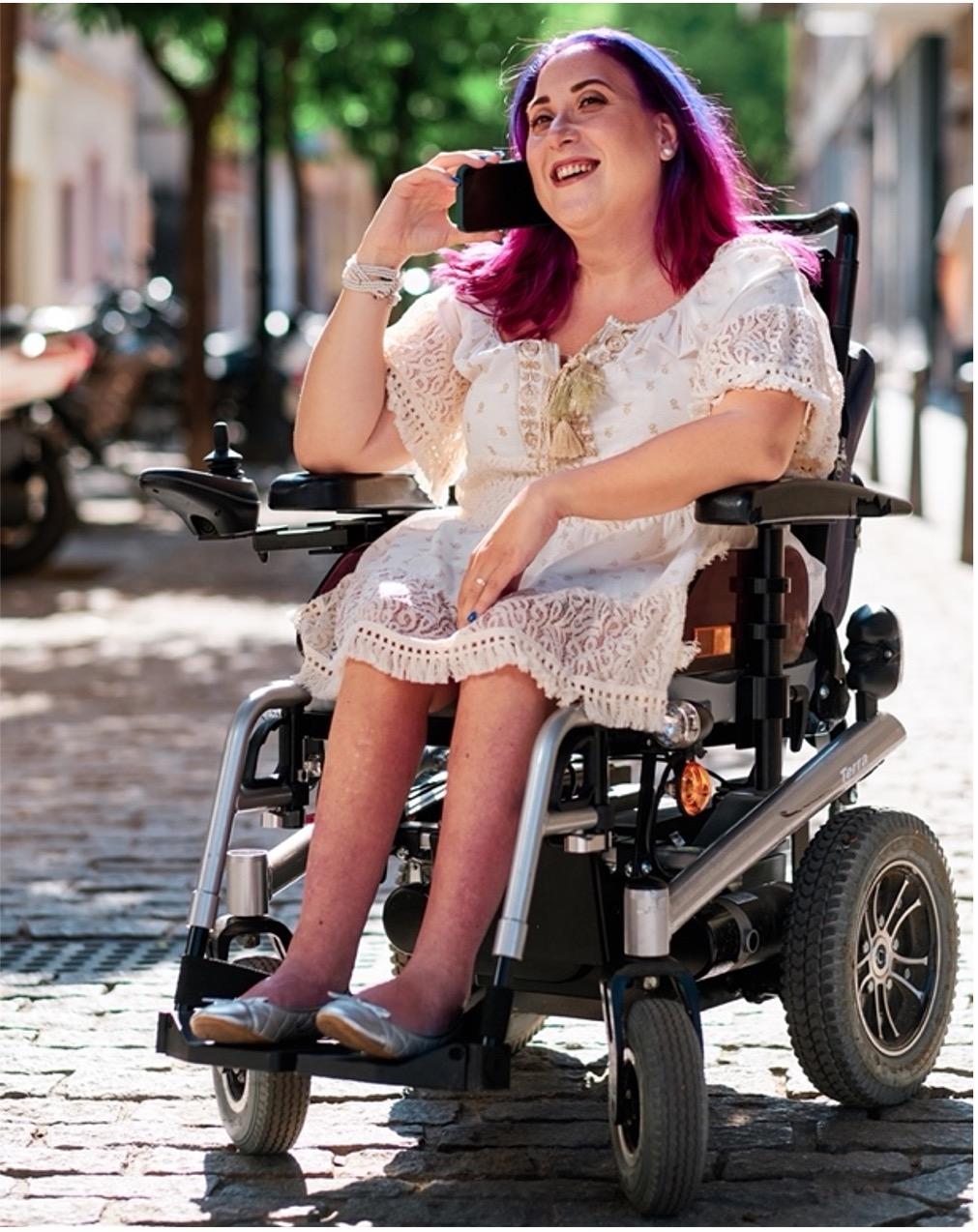 A woman with bright hair in a wheelchair and using her phone.