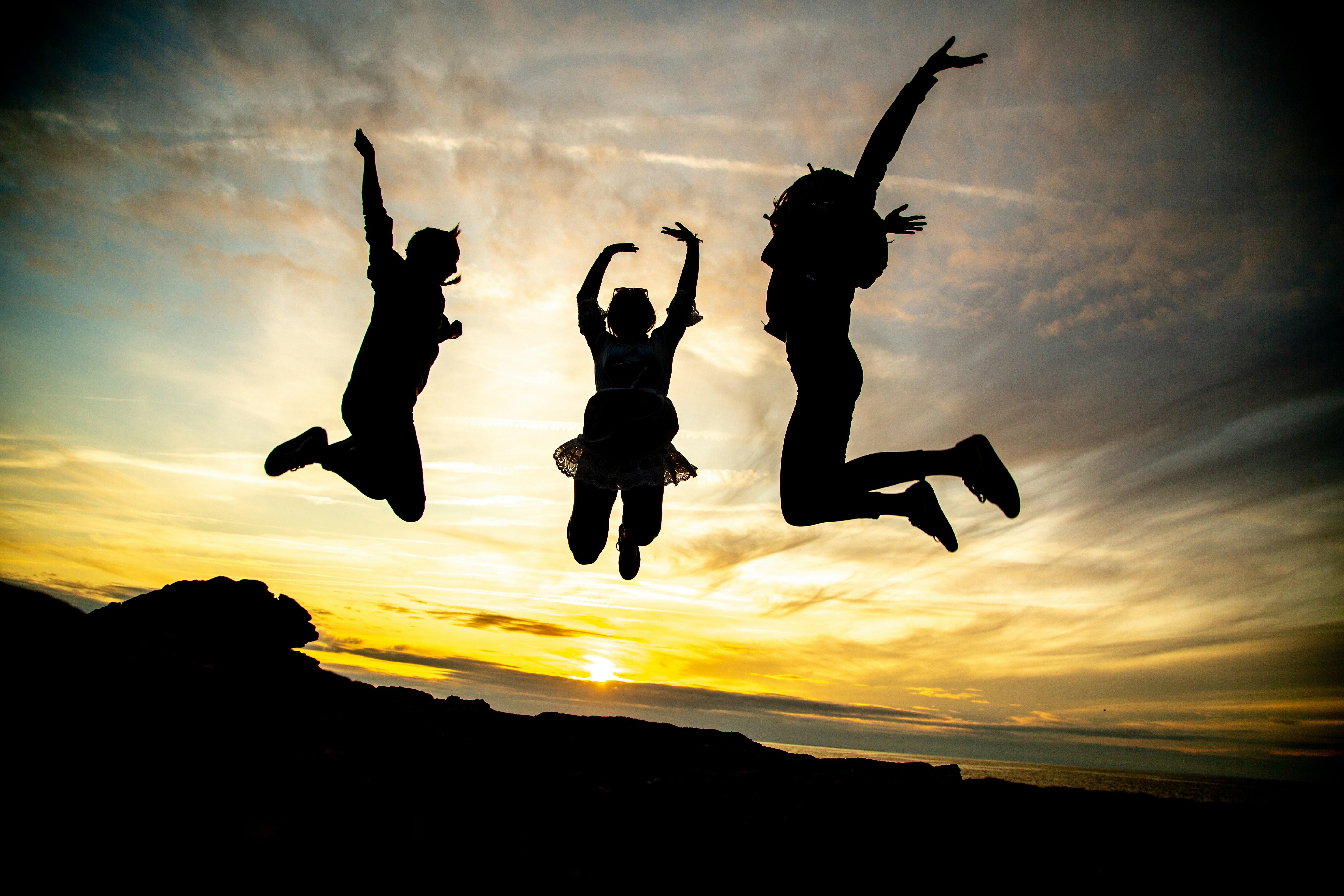 Silhouettes of three children jumping in the air against a backdrop of a sunset